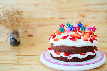 Homemade chocolate whipping cream with strawberry fruit cake decorate colorful candle on wooden table background and flower in vase , Happy Birthday party concept.