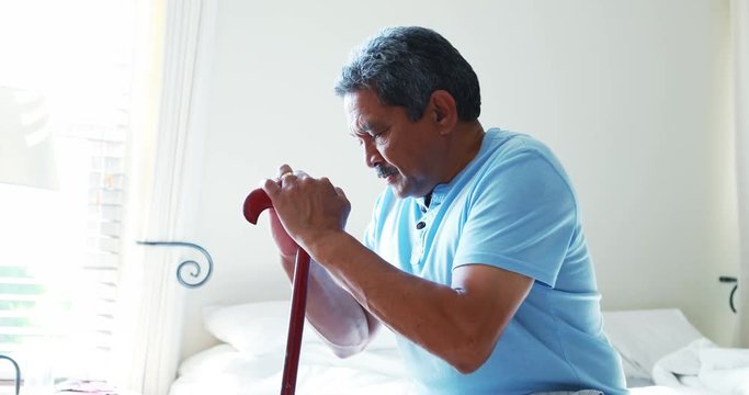 Senior man sitting with walking stick in bedroom 