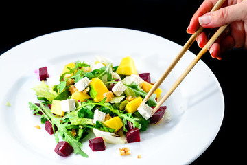 Process of eating delicious and appetizing salad with beetroot and fruit mango in a white plate on black background. Autumn menu in an Italian restaurant.