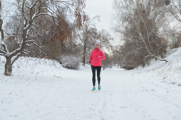 Winter running in park: happy active woman runner jogging in snow, outdoor sport and fitness concept
