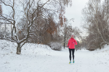 Fototapeta na wymiar Winter running in park: happy active woman runner jogging in snow, outdoor sport and fitness concept 