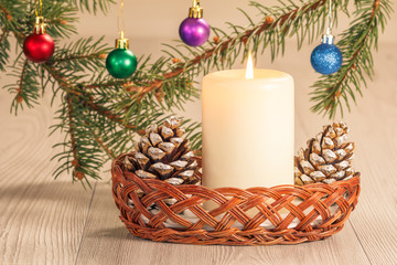 Burning candle, cones and natural fir tree branches with Christmas ornament on wooden boards