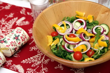 Lovely wooden bowl of salad, with red onion, yellow pepper, baby tomatoes and rocket, on a festive table laid for Christmas dinner