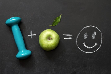 Diet and fitness concept with apple and dumbbell on blackboard
