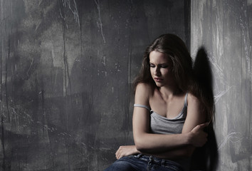 Battered sad woman sitting alone near grey wall