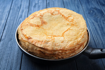 Frying pan with stack of delicious thin pancakes on wooden background