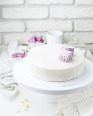 Photo of a creamy white mousse cake with marshmallows in a cafe. A modern cake with a cut piece. Light background, white brick wall, light dishes and cake stand. The atmosphere of the coffee house. 