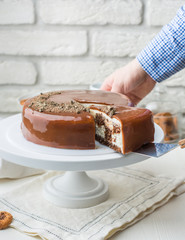 Photo of a chocolate caramel cake in a cafe. A modern cake with a cut piece. Light background, white brick wall, light dishes and cake stand. The atmosphere of the coffee house. Beautiful sweet photo