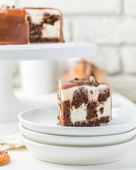 Photo of a chocolate caramel cake in a cafe. A modern cake with a cut piece. Light background, white brick wall, light dishes and cake stand. The atmosphere of the coffee house. Beautiful sweet photo