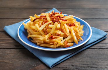 Plate with French fries and bacon on wooden table