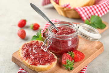 Jar and piece of bread with strawberry jam on table