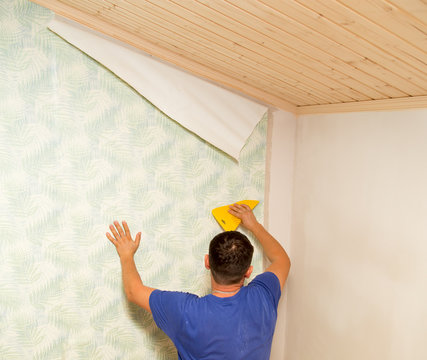 Man glues the wallpaper to the wall in the house
