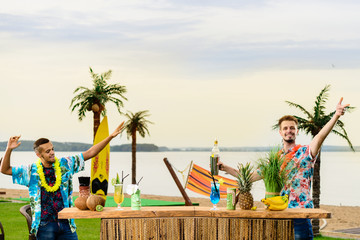 Handsome caucasian bartender and Latin American barman standing near the bar counter and having fun on the ocean. Concept of preparation, relaxing and fun