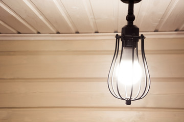 A vintage black lamp under the ceiling in a wooden farmhouse.