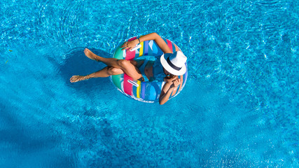Aerial top view of beautiful girl in swimming pool from above, relax swim on inflatable ring donut and has fun in water on family vacation
