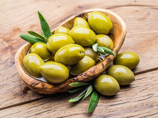 Whole table olives in the wooden bowl on the table.