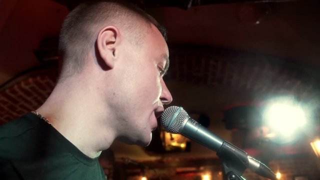 Portrait handsome musician singing song in microphone on rock consert at stage