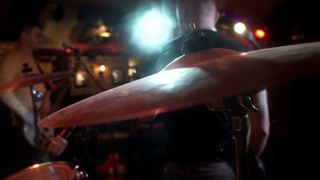 Rock musician plays on electric guitar on background drum plate at consert stage