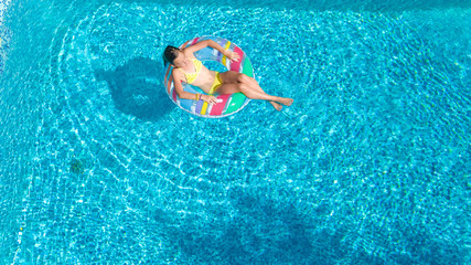 Aerial view of girl in swimming pool from above, kid swim on inflatable ring donut and has fun in water on family vacation
