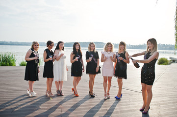 Obraz premium Group of 8 girls wear on black and 2 brides at hen party against sunny beach drinking champagne.