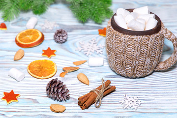 Fototapeta na wymiar Cup of hot Chocolate drink with marshmallows, cinnamon sticks, dry oranges, cones and fir tree on light blue wooden background. Winter christmas holiday background. Flat lay