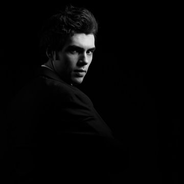 Handsome charismatic man looking serious in dark shadow dramatic light. Black and white portrait. Art