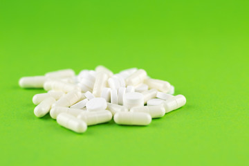 Close up white pills and capsules on green background with copy space. Focus on foreground, soft bokeh. Pharmacy drugstore concept