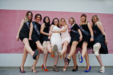 Fototapeta na wymiar Group of 8 girls wear on black and 2 brides at hen party posed against pink wall.