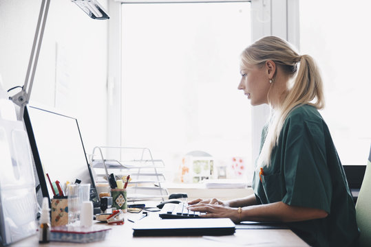 Side View Of Female Nurse Working At Computer Desk Against Window In Office