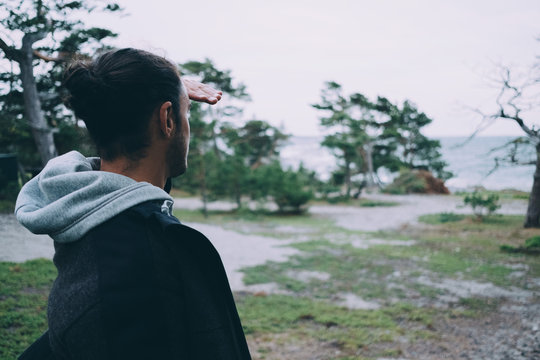 Side view of young man shielding eyes on field at beach