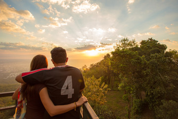 Young couple watching sunrise and hugging in sunlight