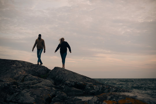 Young Man And Woman Walking On Rocky Hill At Beach