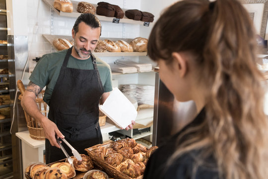 Smiling mature male owner serving fresh bread to female customer at bakery
