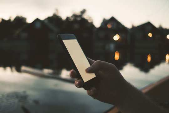 Cropped image of man text messaging through smart phone at lake