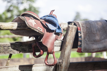 Horse saddle hanging on a wooden fence