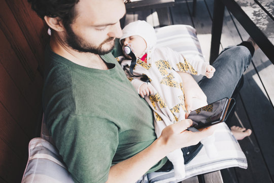 Father with toddler using mobile phone while sitting on chair at holiday villa