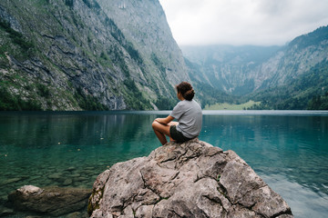 Girl sitting on rock looking at beautiful and misty lake in the