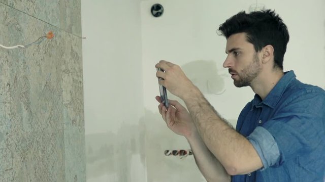 Young man taking photo of tiles with cellphone at his new home
