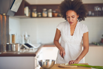 Mixed race woman preparing dinner. Chopping leek while standing in the kitchen