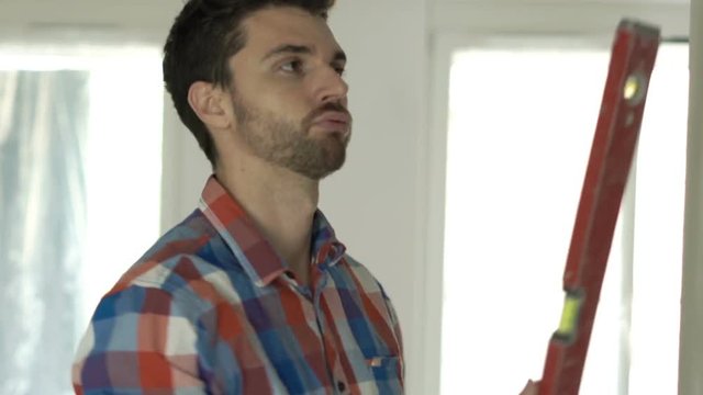 Young man with blueprints checking wall with level at new home 

