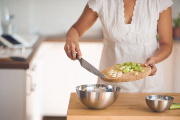 Mixed race woman preparing dinner. Chopping leek while standing in the kitchen