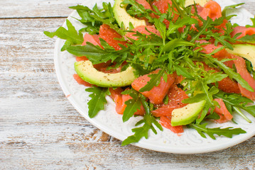 Salad with rocket salad \ arugula, avocado, grapefruit, red fish and mustard sauce on a white wooden background, top view