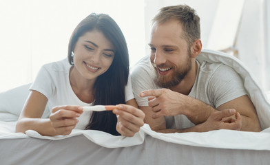 Good news. Handsome man expressing positivity and lying near his girlfriend while pointing at stripe