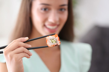 Beautiful young woman with sushi roll at home