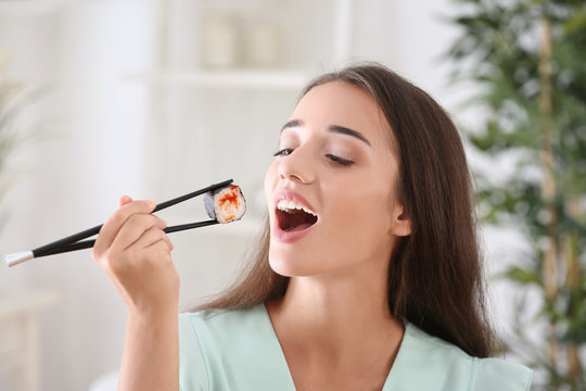Beautiful young woman eating sushi roll at home