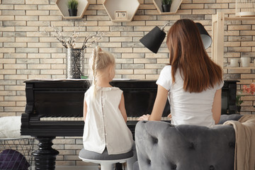 Little girl with teacher learning to play piano indoors