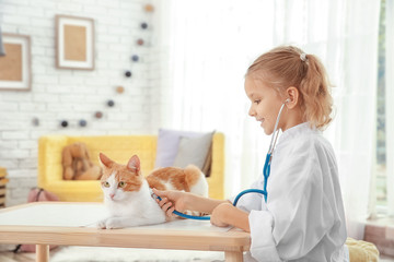 Cute little girl with cat playing doctor at home