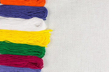 multicolored skeins of embroidery threads on white cotton canvas