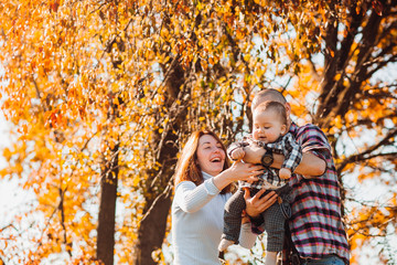 Mom and dad have fun playing with their son under the tree with golden leaves