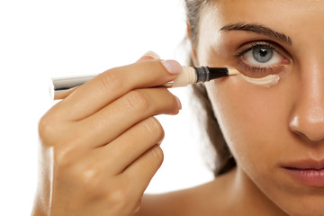 A young woman applies a concealer under the eyes